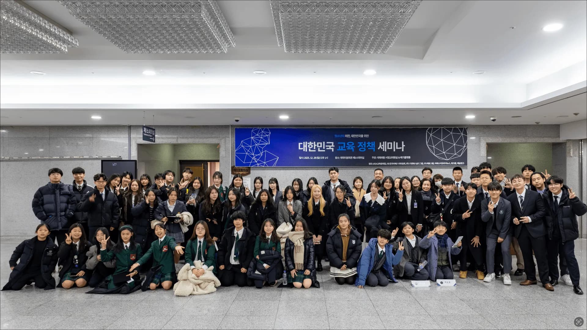 A large group of students poses in a lobby beneath a banner for a Korean education policy seminar.
