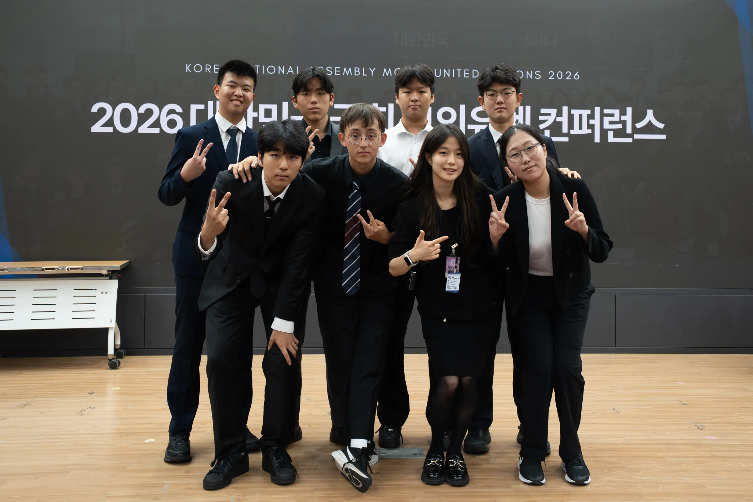 A group of students in suits poses on a stage in front of a large screen with the Korean conference title.